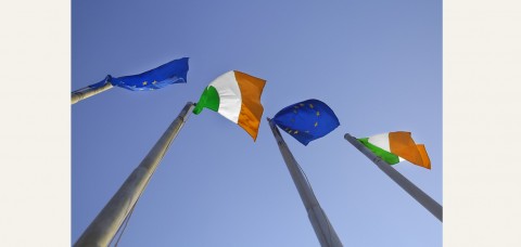 Ireland and EU flags seen from below against a blue sky