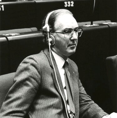 Black and white photograph of Brendan Halligan, a former Member of Seanad Éireann. He is wearing audio headphones while participating in a plenary parliamentary session.