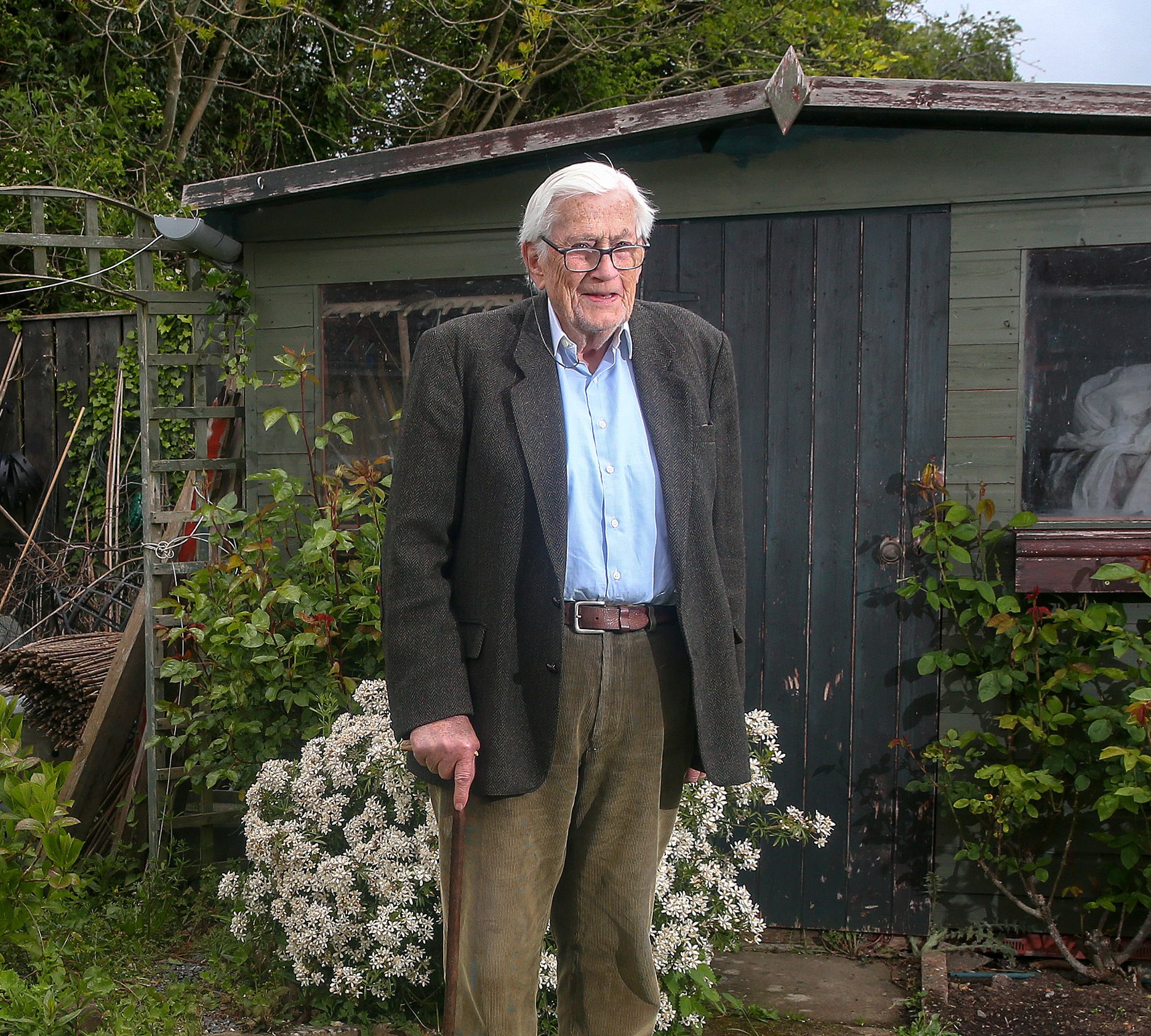 Colour full-length photograph of Seamus Mallon, a former Member of Seanad Éireann, standing in a garden.