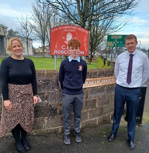 Photo of two teachers and student in front of school sign