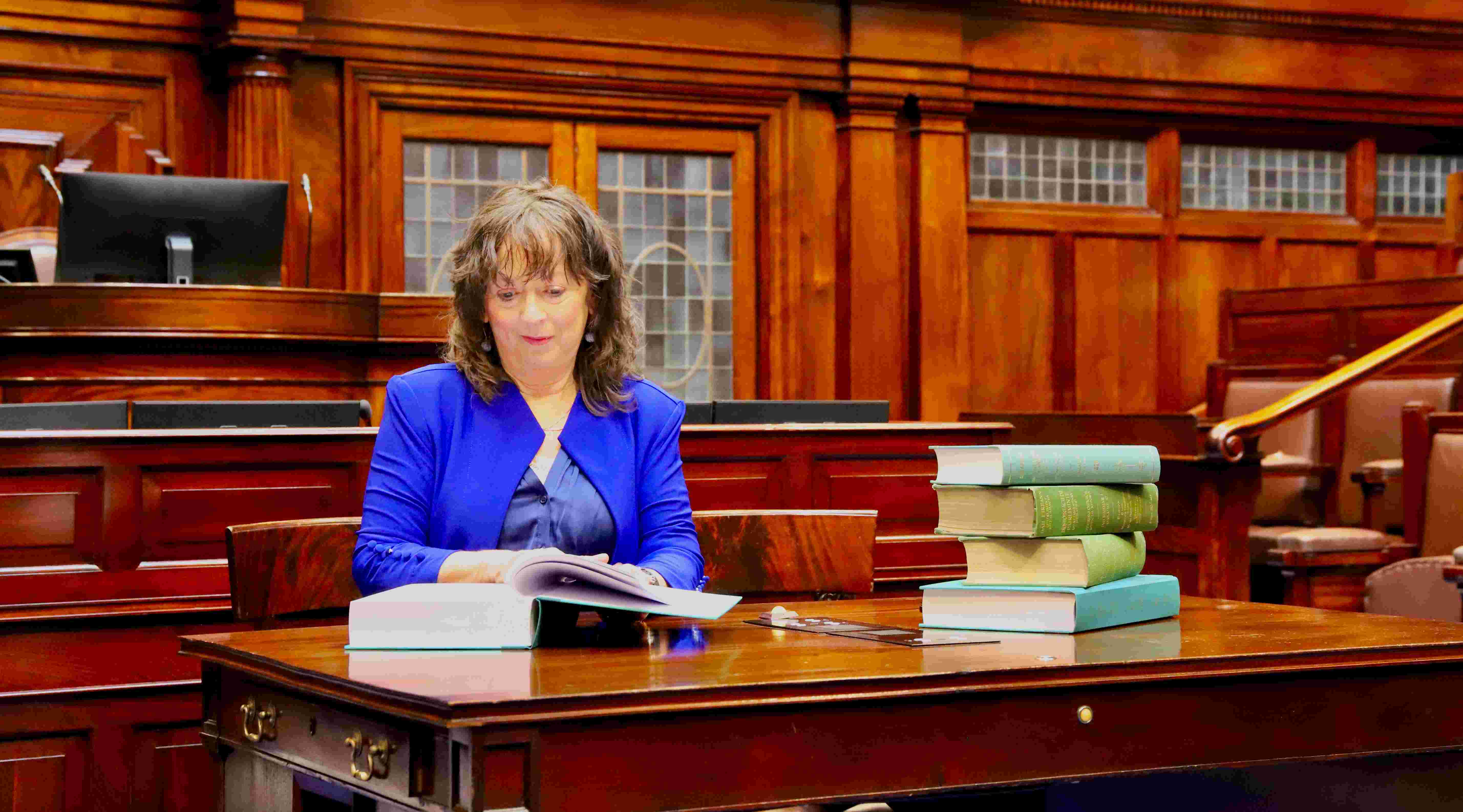 The Editor of Debates and Chief Report examines a copy of the 1,000th bound volume of the Official Report sitting at the reporters' desk in the Dáil Chamber